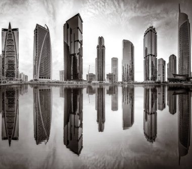 Tek renkli şehir gökdelenleri bulutlu bir gökyüzü altında sakin suyu yansıtan gökdelenler, kentsel gelişim konsepti, Dubai Marina Körfezi BAE