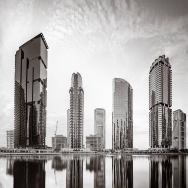 Tek renkli şehir gökdelenleri bulutlu bir gökyüzü altında sakin suyu yansıtan gökdelenler, kentsel gelişim konsepti, Dubai Marina Körfezi BAE