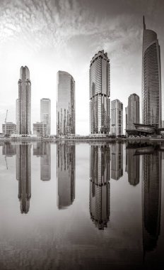 Tek renkli şehir gökdelenleri bulutlu bir gökyüzü altında sakin suyu yansıtan gökdelenler, kentsel gelişim konsepti, Dubai Marina Körfezi BAE