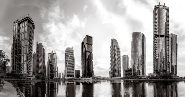 Tek renkli şehir gökdelenleri bulutlu bir gökyüzü altında sakin suyu yansıtan gökdelenler, kentsel gelişim konsepti, Dubai Marina Körfezi BAE