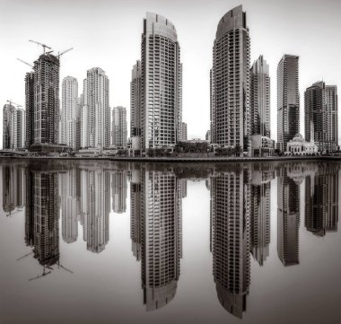 Tek renkli şehir gökdelenleri bulutlu bir gökyüzü altında sakin suyu yansıtan gökdelenler, kentsel gelişim konsepti, Dubai Marina Körfezi BAE