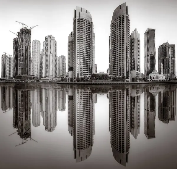 Tek renkli şehir gökdelenleri bulutlu bir gökyüzü altında sakin suyu yansıtan gökdelenler, kentsel gelişim konsepti, Dubai Marina Körfezi BAE