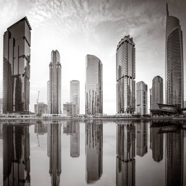 Tek renkli şehir gökdelenleri bulutlu bir gökyüzü altında sakin suyu yansıtan gökdelenler, kentsel gelişim konsepti, Dubai Marina Körfezi BAE