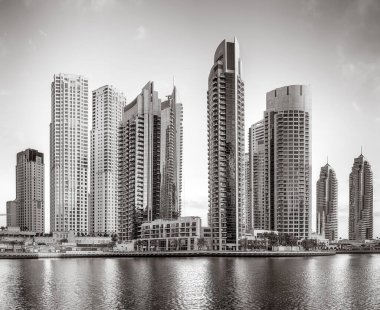 Tek renkli şehir gökdelenleri bulutlu bir gökyüzü altında sakin suyu yansıtan gökdelenler, kentsel gelişim konsepti, Dubai Marina Körfezi BAE