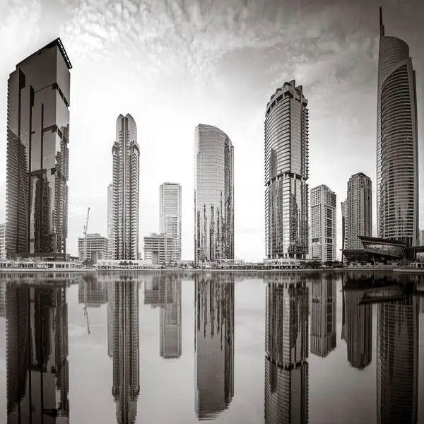 Tek renkli şehir gökdelenleri bulutlu bir gökyüzü altında sakin suyu yansıtan gökdelenler, kentsel gelişim konsepti, Dubai Marina Körfezi BAE