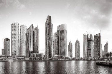 Tek renkli şehir gökdelenleri bulutlu bir gökyüzü altında sakin suyu yansıtan gökdelenler, kentsel gelişim konsepti, Dubai Marina Körfezi BAE