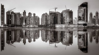 Tek renkli şehir gökdelenleri bulutlu bir gökyüzü altında sakin suyu yansıtan gökdelenler, kentsel gelişim konsepti, Dubai Marina Körfezi BAE