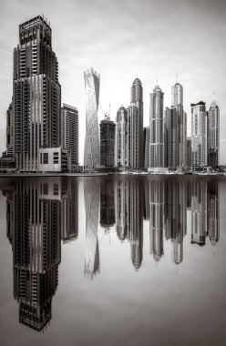 Tek renkli şehir gökdelenleri bulutlu bir gökyüzü altında sakin suyu yansıtan gökdelenler, kentsel gelişim konsepti, Dubai Marina Körfezi BAE