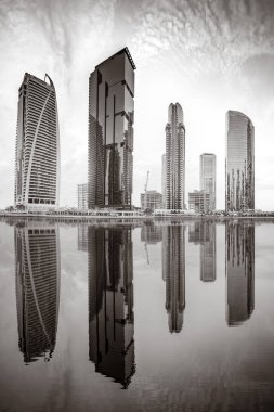 Tek renkli şehir gökdelenleri bulutlu bir gökyüzü altında sakin suyu yansıtan gökdelenler, kentsel gelişim konsepti, Dubai Marina Körfezi BAE