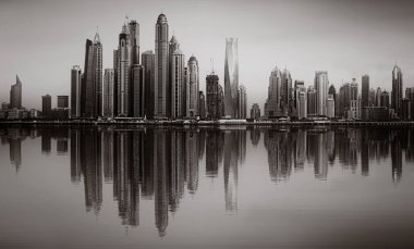 Tek renkli şehir gökdelenleri bulutlu bir gökyüzü altında sakin suyu yansıtan gökdelenler, kentsel gelişim konsepti, Dubai Marina Körfezi BAE