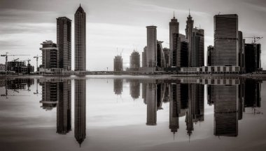 Tek renkli şehir gökdelenleri bulutlu bir gökyüzü altında sakin suyu yansıtan gökdelenler, kentsel gelişim konsepti, Dubai Marina Körfezi BAE