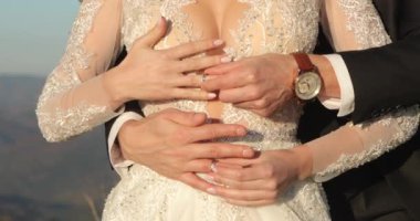 Gelin ve damat mavi gökyüzünün altında kucaklaşır ve parmaklarına alyans takarlar..