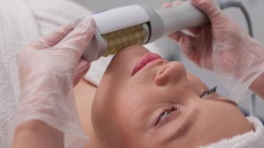Gözleri kapalı bir kadın güzellik salonunda kaldırma makinesi masajı alıyor. Bir kadın bir kozmetikçiden canlandırıcı bir yüz bakımı alır.