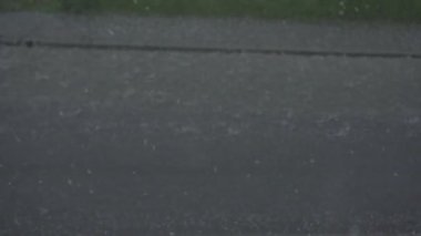 Slow motion close-up of heavy raindrops on a wet road as a motorcycle passes by