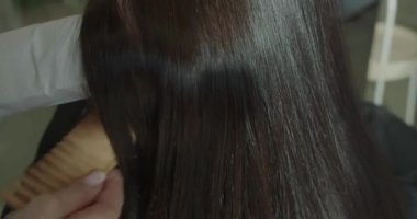 Düzleştirdikten sonra düz ve ipeksi esmer saçların ve keratin tedavisinin gösterimi. Kuaför, güzellik salonunu düzelttikten sonra parlak ve ipeksi bir tutam esmer saçı gösteriyor.