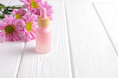 Cosmetic bottle with pink daisy flowers on wooden table, copy space