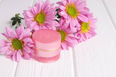 Cosmetic bottle with pink daisy flowers on wooden table, copy space