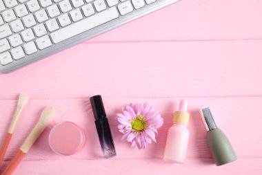 Bottles of cosmetic with flowers and keyboard on pink table