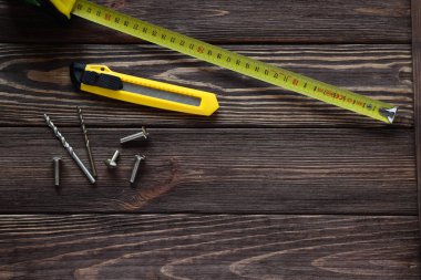 Teyp ölçüsü, inşaat bıçağı, tahta masaya vidalar, iş aletleri.