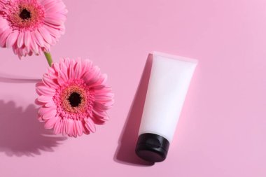 Beyaz boş tüp, cilt bakım kremi, losyon şişesi pembe çiçeklerle süslenmiş.