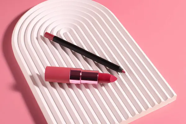 Pink lipstick and lip liner pencil on wavy podium, copy space