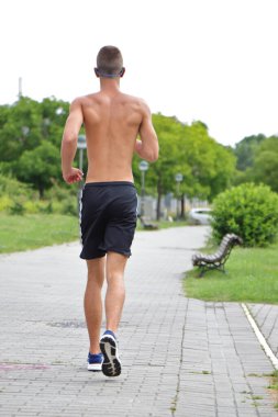 Şehir parkında koşan genç bir adam, sokaklarda kulaklıkla koşan bir genç, hareket halinde.