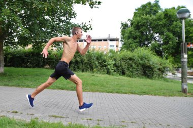 Şehir parkında koşan genç bir adam, sokaklarda kulaklıkla koşan bir genç, hareket halinde.
