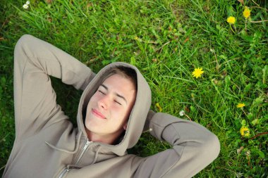 Gülümseyen, pozitif ergen portresi, yeşil çimlerin üzerinde yatan genç adam.