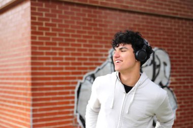 Kulaklıklı Latin ergen midesi sokakta yürürken müzik dinliyor, gelişigüzel ergen bir çocuk.