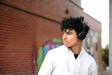 Kulaklıklı Latin ergen midesi sokakta yürürken müzik dinliyor, gelişigüzel ergen bir çocuk.