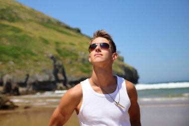 Beyaz kolsuz tişörtlü, güneş gözlüklü, yaz plajında bronz tenli, sıradan bir genç kız.