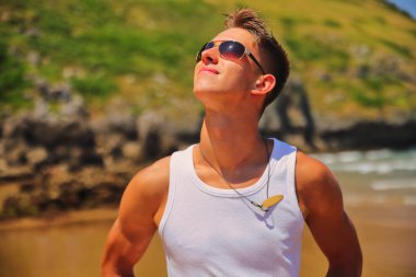 Beyaz kolsuz tişörtlü, güneş gözlüklü, yaz plajında bronz tenli, sıradan bir genç kız.