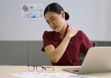 Genç Asyalı iş kadını eliyle omzunu tutuyor. Uzun süreli bilgisayar kullanımının acısını dindirmek için..