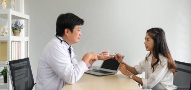 Beyaz cüppeli ve steteskoplu Asyalı dişçi diş modelini işaret ederek genç hastaya diş ve diş tellerini açıklar. Sakız ağrısını azaltır. Sağlık ve Tıp Konsepti. 