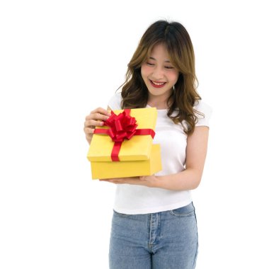 Beyaz tişörtlü ve kot pantolonlu genç Asyalı kadın özel bir durum için hediye kutusunu açıyor. Beyaz arkaplanda stüdyo ışığı olan bir portre.