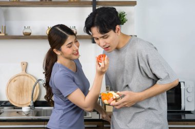 Asyalı çift mutfakta birlikte vakit geçiriyor. Genç bir kadın erkek arkadaşını salata kasesinden bir parça domates ile besliyor..