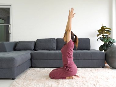Ev ödevi sırasında elmas poz egzersizi yapan Asyalı ev hanımı. Vajrasana 'da yoga yapan kadın oturma odasındaki halıya poz veriyor..