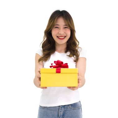 Beyaz tişörtlü ve kot pantolonlu genç Asyalı kadın önünde bir hediye kutusu sunuyor. Beyaz arkaplanda stüdyo ışığı olan bir portre.