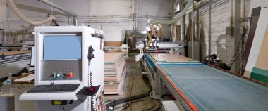 Endüstriyel fabrikada klavye ve fareyle ahşap mobilya parçaları üreten mavi ekran sistem kontrol dolabı.