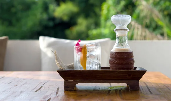 Start Up, mocktail drinks add the mixture with raspberry, jasmine and thaitea. A glass of ice, orange peel and wildflowers place next to a tall glass pitcher. Cold drink served on wooden tray.