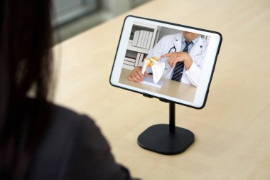 Back view of woman in suit have webcam conference on tablet computer with doctor about shoulder bone joint treatment. Healthcare and medicine concept.