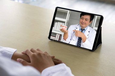 Back view of woman in white gown sit at desk have webcam conference on tablet computer with asian dentist about orthodontics and braces. Healthcare and medicine concept.