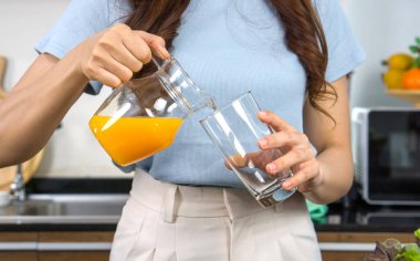 Closeup female hand pour mixed fruit and veggie smoothie from Jar into glass.