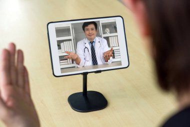 Takım elbiseli adamın arka planda Asyalı doktorla web kamerası konferansı var..