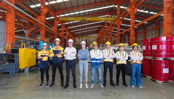 Group of male and female factory labor stand smiling together with arms crossed in industry factory. Everyone wearing safety uniform and helmet. Workers working in the metal sheet factory.