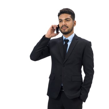 Siyah takım elbiseli, bıyıklı ve sakallı genç iş adamı elini cebine sokarken cep telefonu kullanıyor. Beyaz arka planda stüdyo ışıklandırmalı bir portre. İzole edilmiş 
