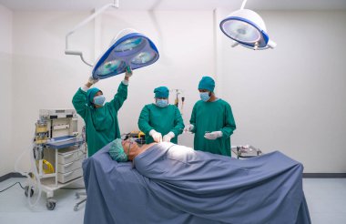 Hemşire ameliyat ışıklarını ayarlıyor. Bir grup cerrah ve hemşire ameliyat odasında ameliyat için ameliyat elbisesi giyiyorlar..