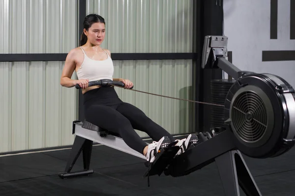 Spor giyimli atletik bir kadın, iyi donanımlı bir spor salonundaki kürek çekme makinesinde yoğun bir antrenman yapıyor. Sağlık ve aktif yaşam tarzı kavramı
