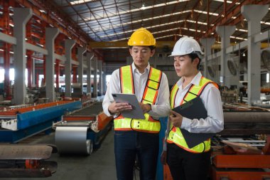İki tetikte inşaat işçisi, çalkantılı bir fabrika zemininde, dijital tableti dikkatle inceleyerek kritik proje detaylarını tartışıyor..