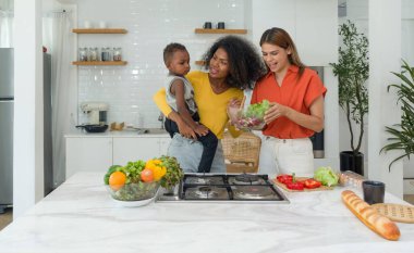 İki farklı lezbiyen kadın evde bir mutfakta vakit geçiriyorlar. Uyumlu bir şekilde yemek hazırlama görevlerini paylaşıyorlar. Aynı zamanda da bir bebeği büyütüyorlar..